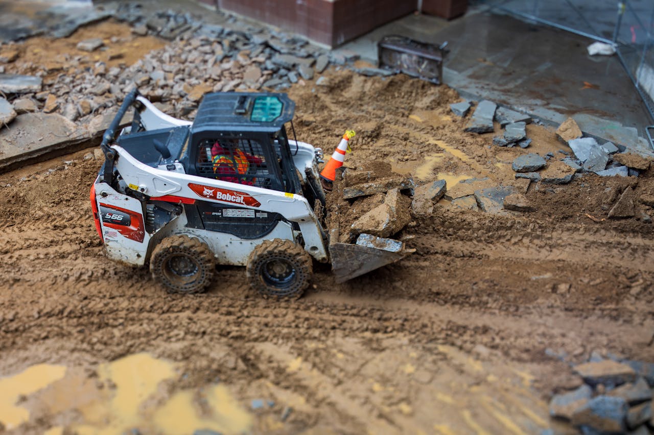 A skid steer loader moves rocks on a muddy construction site, showcasing construction machinery in action.